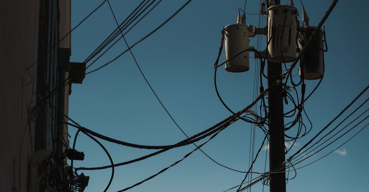 Low angle view of power lines and transformers against a clear blue sky, depicting modern electricity infrastructure.